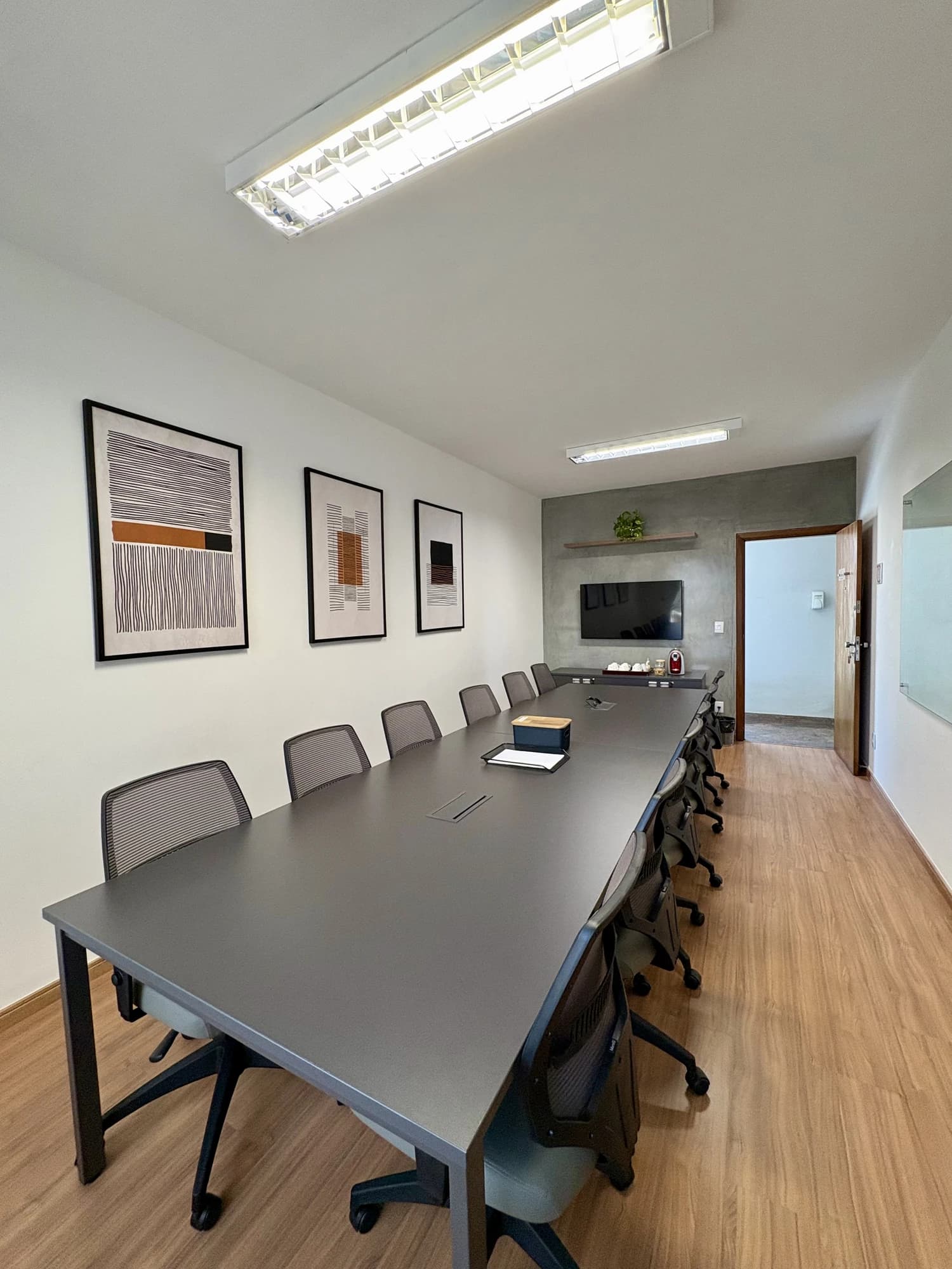 Perspectiva vertical da mesa de reunião com quadro de vidro e TV na parede cinza